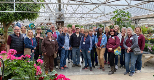 Sedgwick County Extension Master Gardeners posed for a picture in a greenhouse with flowers blooming around them.